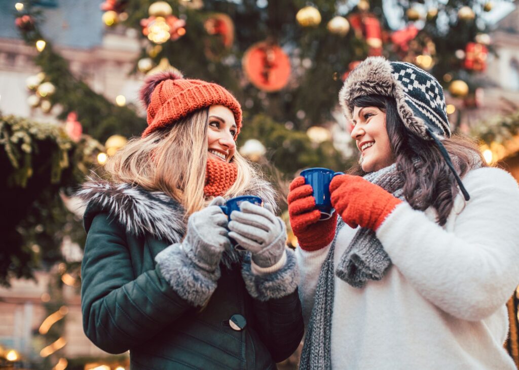 Zwei warm angezogene Frauen mit Glühwein vor Christbaum