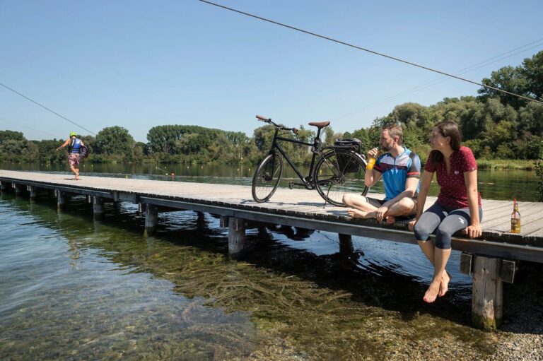 Mann und Frau sitzen auf Steg am Wasser mit Rad