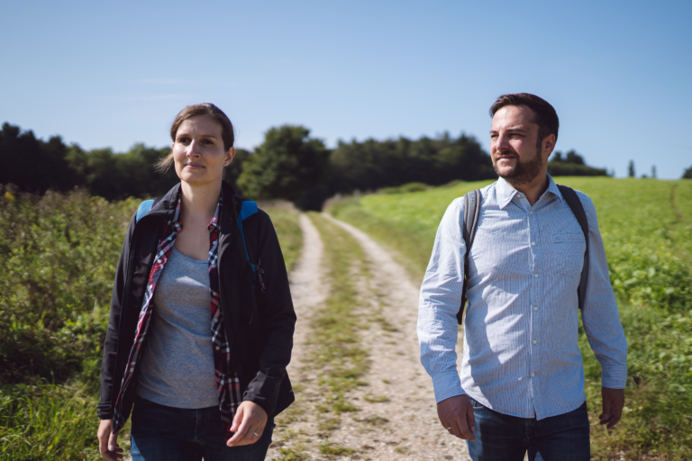 Frau und Mann auf Wanderweg mit Wald im Hintergrund